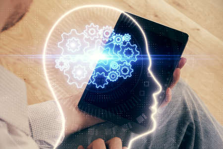 Double exposure of man's hand holding and using a digital device and brain hologram drawing. Data...