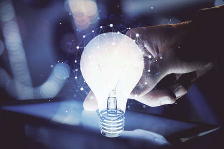 Double exposure of man's hands holding and using a digital device and bulb hologram drawing. Idea...