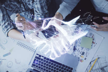Double exposure of handshake hologram and man and woman working together holding and using a mobile...