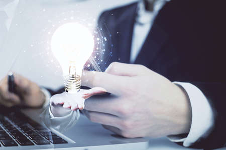 Double exposure of man's hands holding and using a digital device and bulb hologram drawing. Idea concept.の写真素材