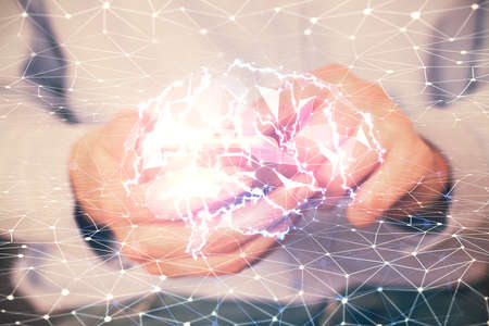 Double exposure of man's hand holding and using a digital device and brain hologram drawing. Data...
