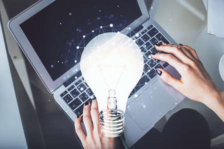 Double exposure of woman hands working on computer and light bulb hologram drawing. Top View. Idea...