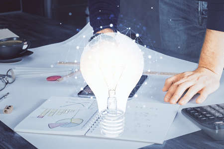 Double exposure of man's hands holding and using a digital device and bulb hologram drawing. Idea...