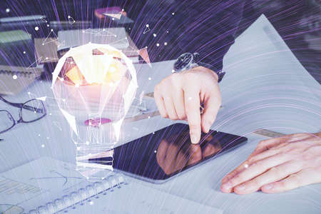 Double exposure of man's hands holding and using a digital device and bulb hologram drawing. Idea...