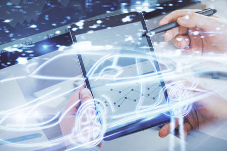 Double exposure of man's hands holding and using a digital device and automobile theme hologram drawing. Technology concept.の写真素材