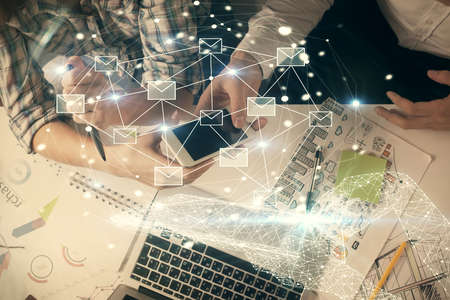 Double exposure of envelop theme hologram and man and woman working together holding and using a...