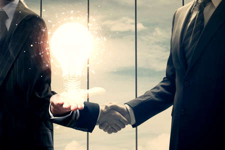 Double exposure of light bulb hologram and handshake of two men. Idea concept.の写真素材