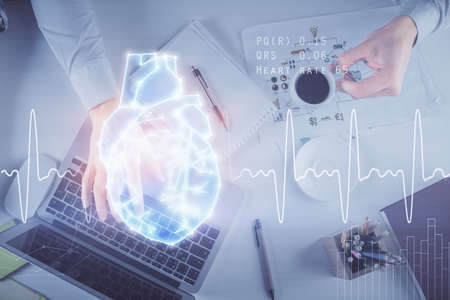 Double exposure of man's hands typing over computer keyboard and human heart hologram drawing. Top view. Medical education concept.の写真素材
