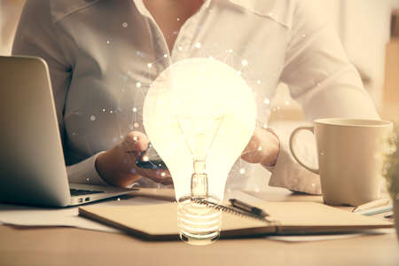 Double exposure of light bulb hologram and woman holding and using a mobile device. Idea concept.