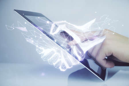 Double exposure of man's hands holding and using a digital device and handshake drawing. Partnership concept.の写真素材