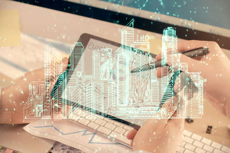 Double exposure of man's hands holding and using a digital device and city drawing.