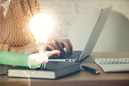 Double exposure of woman hands typing on computer and light bulb drawing. Idea concept.の写真素材