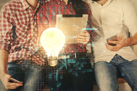 Double exposure of bulb hologram and man and woman working together holding and using a mobile device. Idea conceptの写真素材