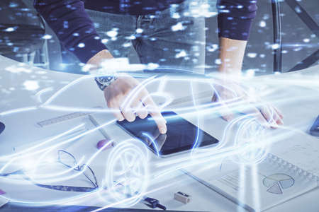 Double exposure of man's hands holding and using a digital device and automobile theme hologram...