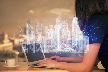 Double exposure of woman hands typing on computer and buildings drawing. Smart-city concept.の写真素材