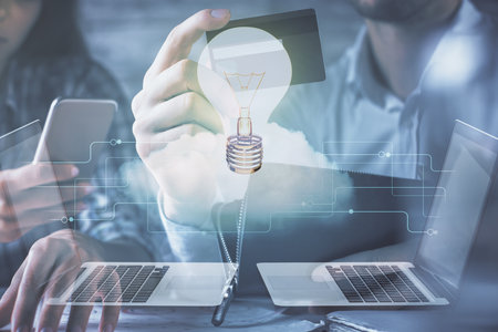 Double exposure of man and woman on-line shopping holding a credit card and light bulb hologram...