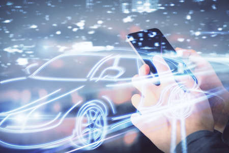 Double exposure of man's hands holding and using a digital device and automobile theme hologram...