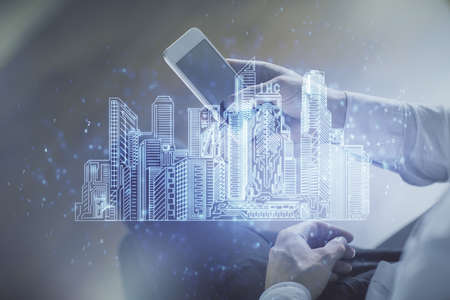Double exposure of man's hands holding and using a digital device and city drawing.