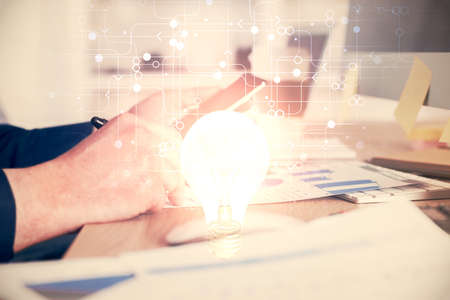 Double exposure of man's hands holding and using a digital device and bulb hologram drawing. Idea...