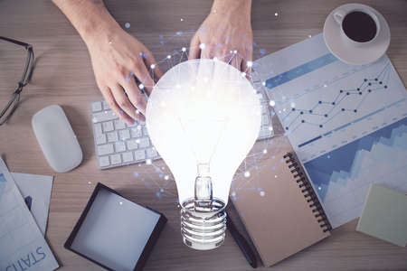 Double exposure of man's hands typing over computer keyboard and bulb hologram drawing. Top view....