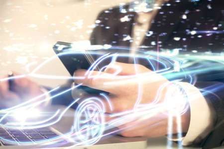 Double exposure of man's hands holding and using a digital device and automobile theme hologram drawing. Technology concept.の写真素材