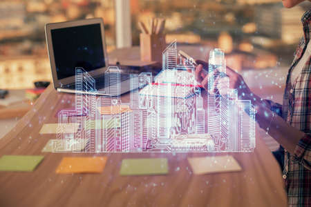 Double exposure of woman hands typing on computer and buildings drawing. Smart-city concept.の写真素材