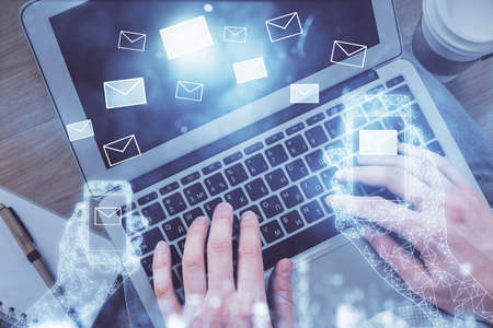 Double exposure of man's hands typing over computer keyboard and flying envelop hologram drawing. Top view. e-mail concept.の写真素材