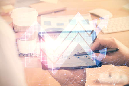 Double exposure of man's hands holding and using a digital device and arrows hologram drawing....
