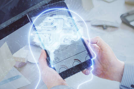Double exposure of man's hand holding and using a digital device and brain hologram drawing. Data...