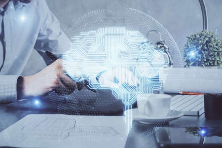 Double exposure of man's hand holding and using a digital device and brain hologram drawing. Data...