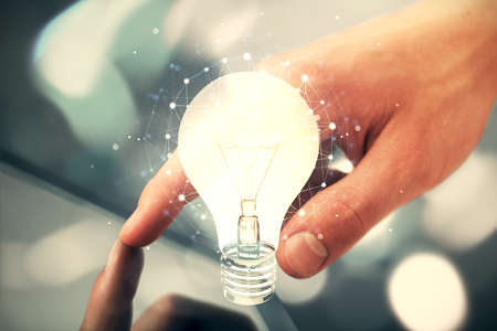 Double exposure of man's hands holding and using a digital device and bulb hologram drawing. Idea...