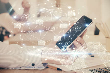 Double exposure of man's hands holding and using a digital device and envelop hologram drawing. E-mail concept.の写真素材