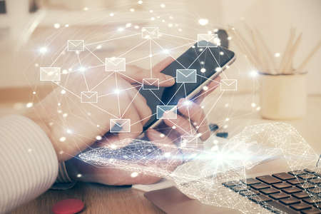 Double exposure of man's hands holding and using a digital device and envelop hologram drawing. E-mail concept.の写真素材