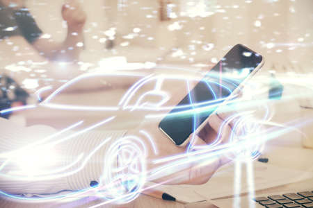Double exposure of man's hands holding and using a digital device and automobile theme hologram...