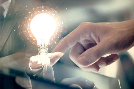 Double exposure of man's hands holding and using a digital device and bulb hologram drawing. Idea concept.の写真素材