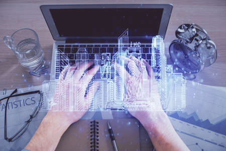 Double exposure of man's hands typing over computer keyboard and buildings drawing. Top view. smart...