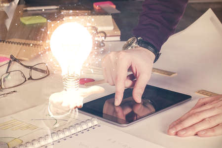 Double exposure of man's hands holding and using a digital device and bulb hologram drawing. Idea concept.の写真素材