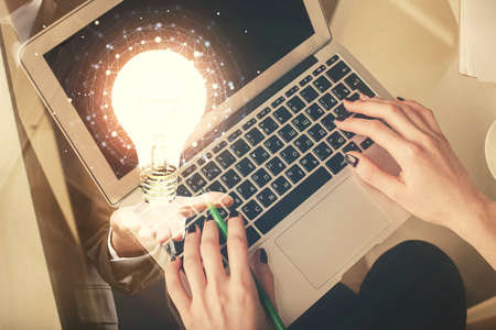 Double exposure of woman hands working on computer and light bulb hologram drawing. Top View. Idea concept.の写真素材