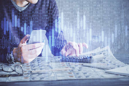 Double exposure of man's hands holding and using a digital device and forex graph drawing. Financial market concept.の写真素材