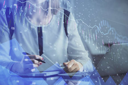 Double exposure of businesswoman hands typing on computer and financial graph hologram drawing....