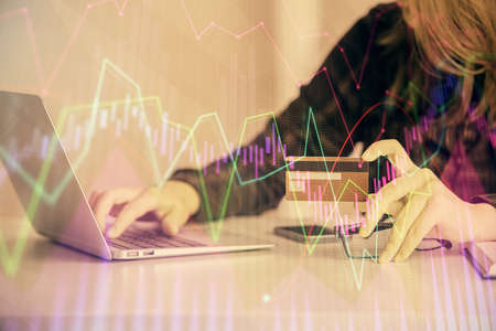 Double exposure of woman on-line shopping holding a credit card and financial graph drawing. Stock...