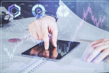 Double exposure of man's hands holding and using a digital device and forex graph drawing. Financial...