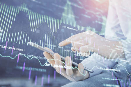 Double exposure of man's hands holding and using a digital device and forex graph drawing. Financial...
