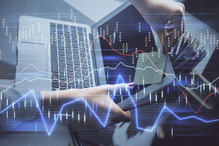 Double exposure of businesswoman hands typing on computer and financial graph hologram drawing....