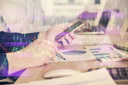 Double exposure of man's hands holding and using a digital device and forex graph drawing. Financial...