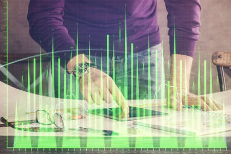 Double exposure of man's hands holding and using a digital device and forex graph drawing. Financial...