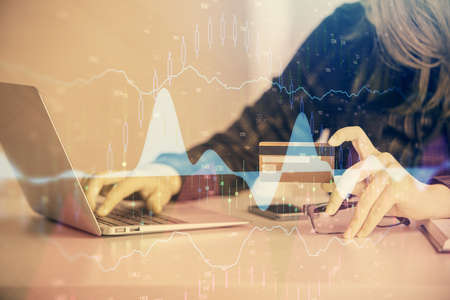 Double exposure of woman on-line shopping holding a credit card and financial graph drawing. Stock...