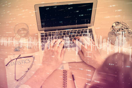 Double exposure of man's hands typing over laptop keyboard and forex chart hologram drawing. Top...