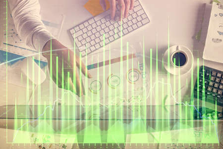 Multi exposure of man's hands typing over computer keyboard and forex graph hologram drawing. Top...