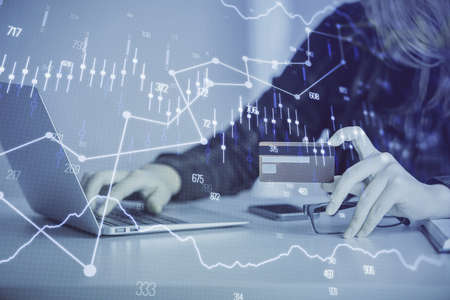 Double exposure of woman on-line shopping holding a credit card and financial graph drawing. Stock...